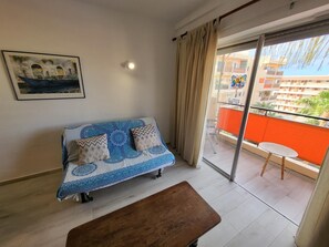 Ein Zimmer mit einer Couch, einer Bank, einem Balkon mit Tisch und einem Bild an der Wand.
