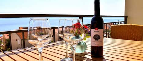 A table with two empty wine glasses and a bottle of Merlot wine on a balcony overlooking the sea.