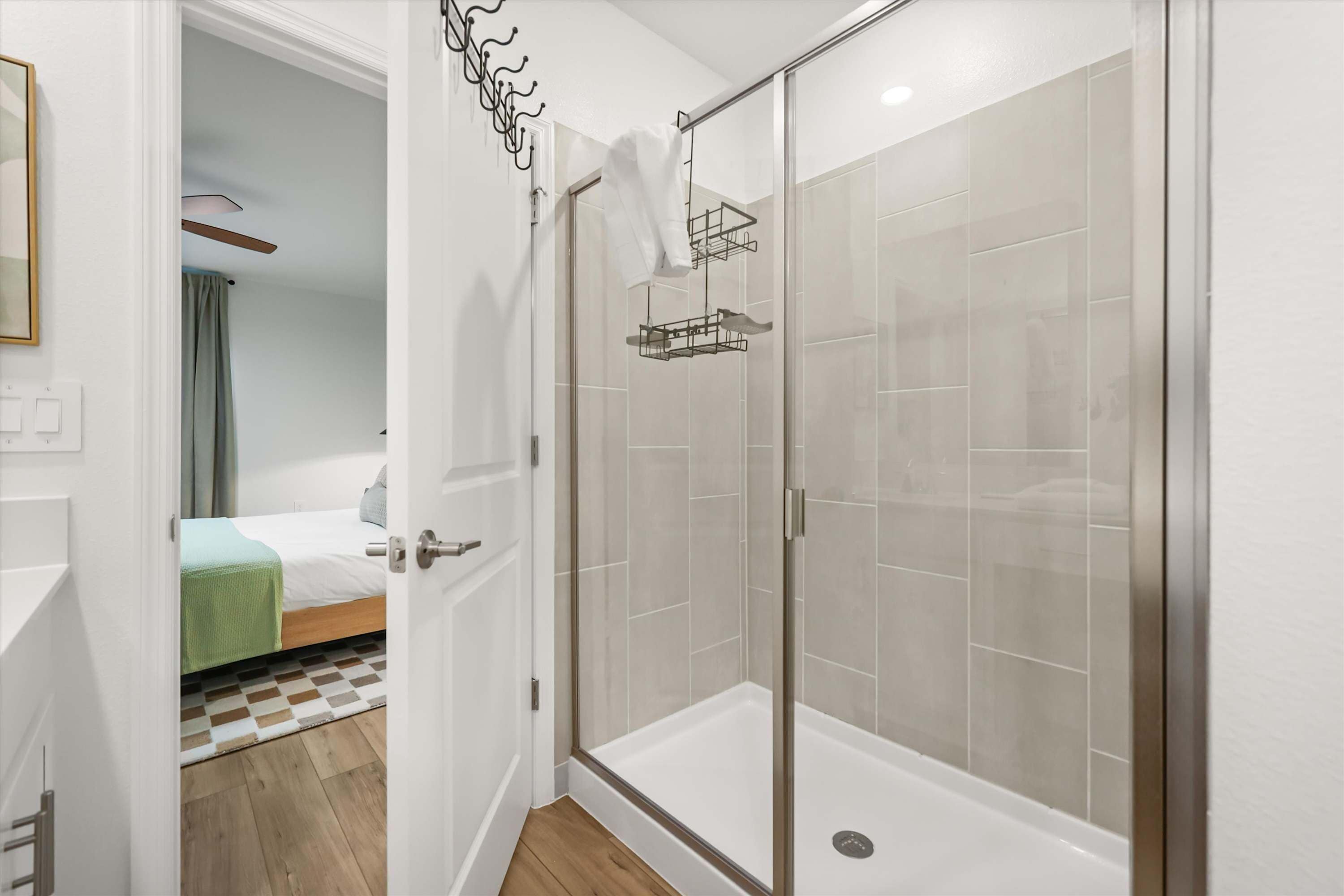 Quarto de hotel com chuveiro, cama com manta verde e chão quadriculado.