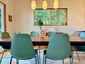 A dining area with a long table, multiple chairs, a vase with a plant, and pendant lights.
