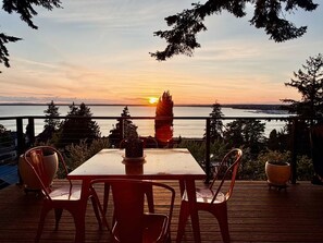 A table and chairs on a wooden deck with a view of the sunset over water. - Luxury Bay Retreat Hot Tub Views (Bellingham)