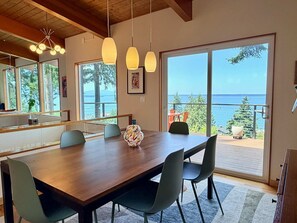 A dining area with a wooden table, four chairs, pendant lights, and a view of the ocean through large sliding doors. - Luxury Bay Retreat Hot Tub Views (Bellingham)