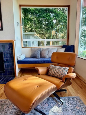 A room with a sofa, a chair, a patterned rug, and a view of trees through a window.