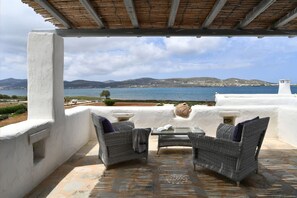 Un espace extérieur aménagé, abrité et doté de mobilier en osier, d’un sol en pierre et offrant une vue sur la mer et les collines.