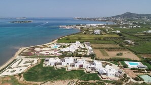 Vue aérienne d’une station balnéaire avec des bâtiments blancs, une plage et une montagne en arrière-plan.