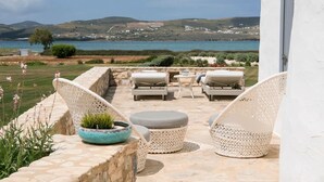 Eine Terrasse mit Korbmöbeln, einer Steinmauer und Blick auf das Meer und die Hügel.