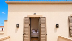 A hotel entrance with a beige exterior, a bed with a brown pillow, and two wall-mounted light fixtures. - Bon Filius - Luxury Private Villa w Pool in Chania (Apokoronas)