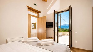 A bedroom with a bed, towels, a TV, and a balcony with a mountain view. - Bon Filius - Luxury Private Villa w Pool in Chania (Apokoronas)