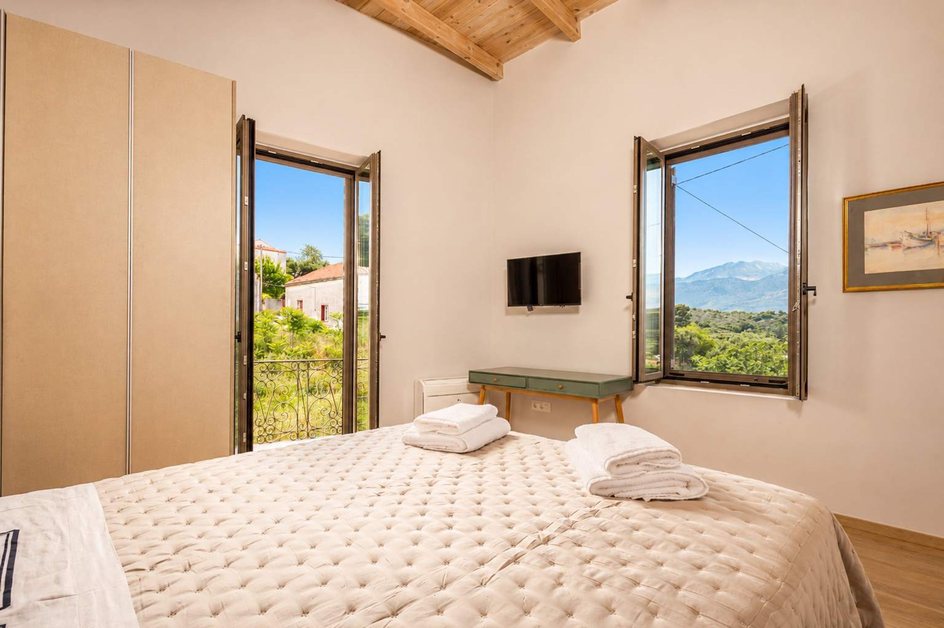 Un dormitorio con cama, televisión, ventana y balcón.