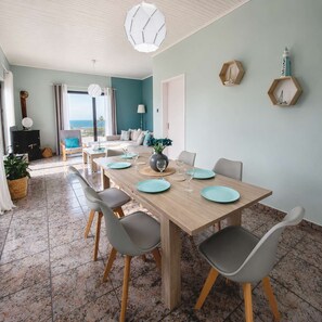 A dining area with a wooden table, grey chairs, and a view of the sea through the window. - Western Sun Near Balos Falassarna (Kissamos)