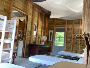 Ein rustikaler Holzraum mit Etagenbett, Schreibtisch, Spiegel, Ventilator und Fenster.
