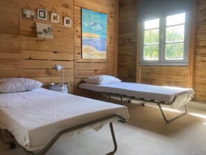 Ein Zimmer mit zwei Betten, einem Nachttisch mit Lampe, Holzwänden, einem Gemälde und einem Fenster mit Blick.