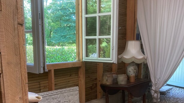 A rustic room with a wooden chest, a table with a lamp, and a view of greenery through a window. - Holiday Home “Dormitory in Charente” with Private Terrace and Shared Garden (Jarnac)