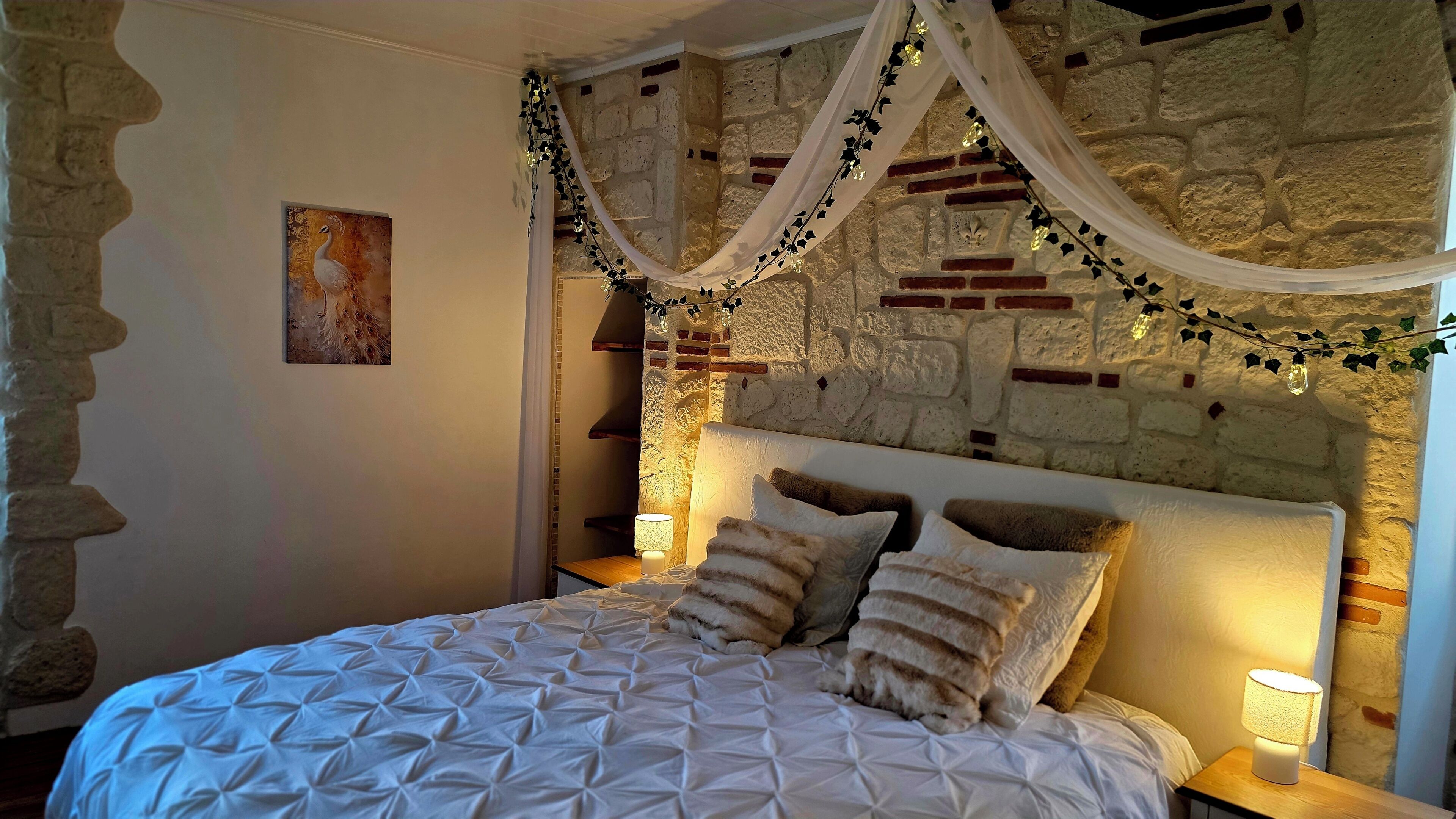 Ein Schlafzimmer mit einer Steinwand, einem Bett mit weißer Steudecke und zwei Nachttischlampen.