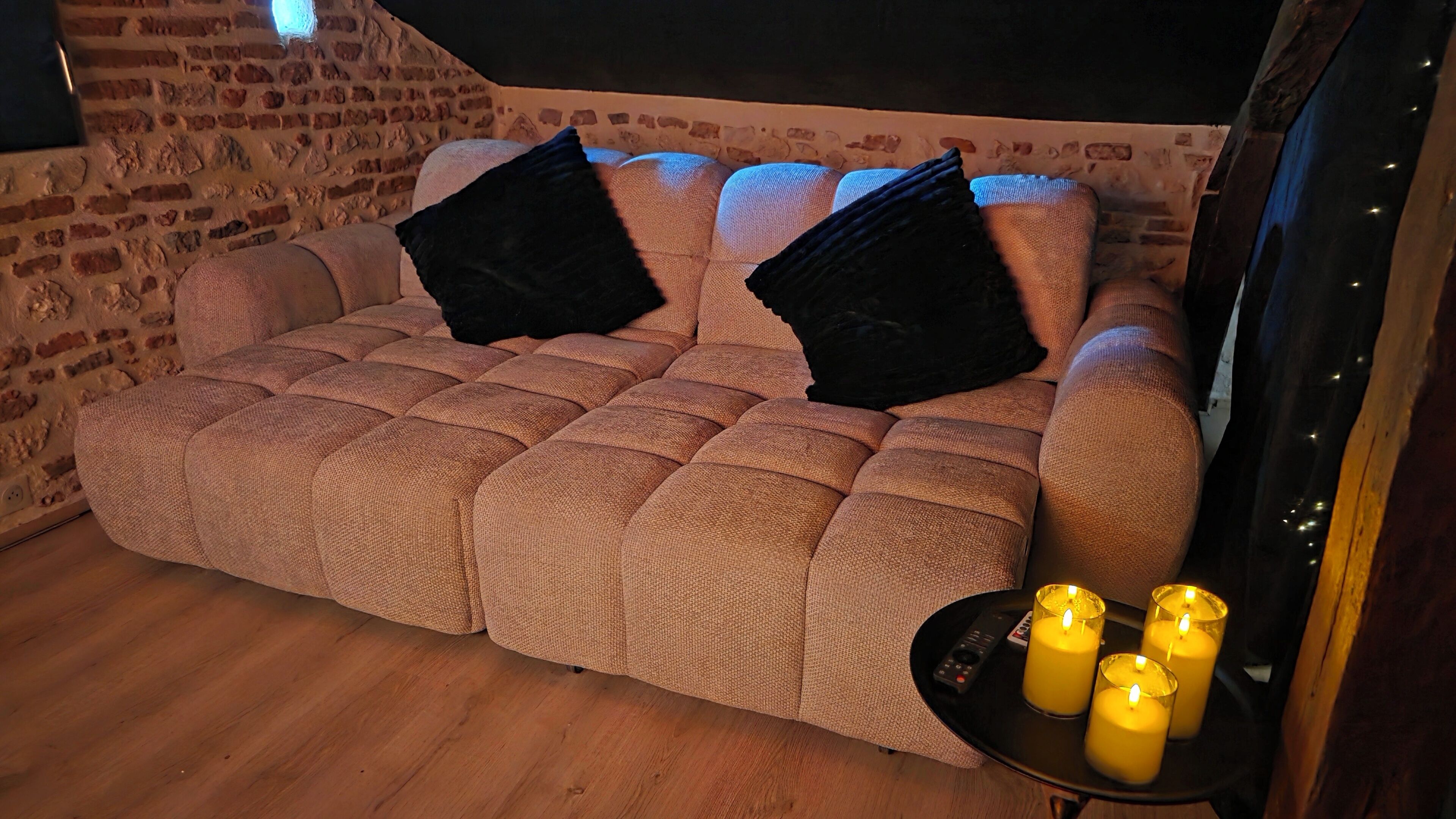 Um quarto acolhedor com uma parede de tijolos, um sofá estofado com almofadas pretas e uma mesinha com velas.
