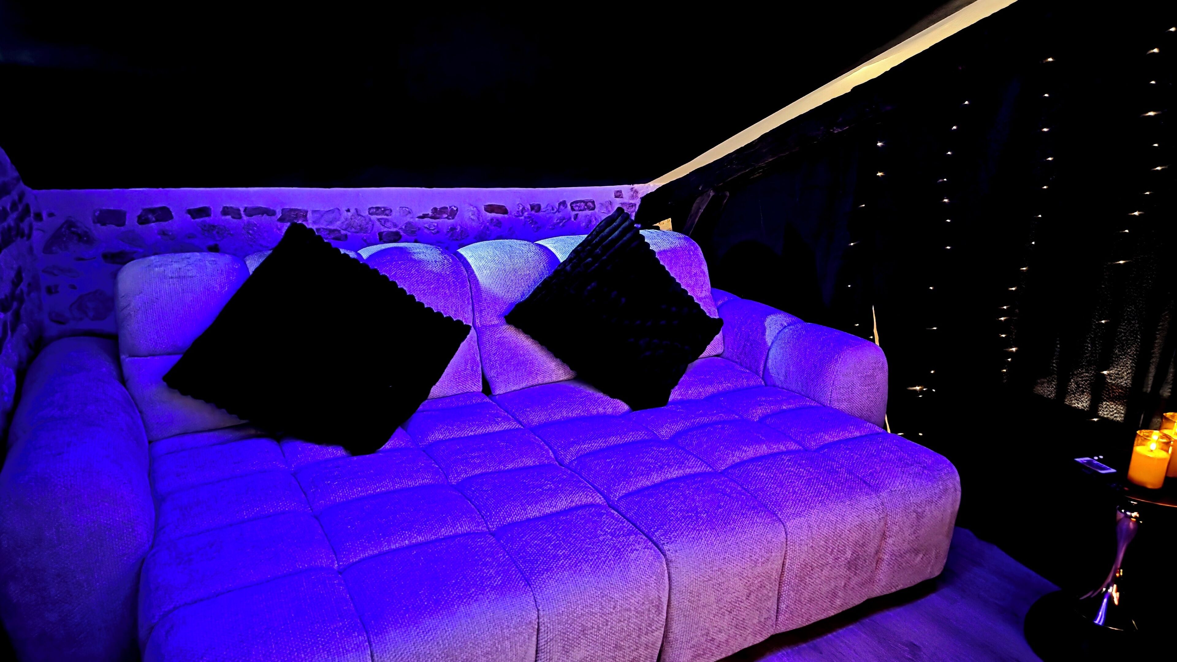 A room with a sofa, two pillows, a stone wall, and string lights.