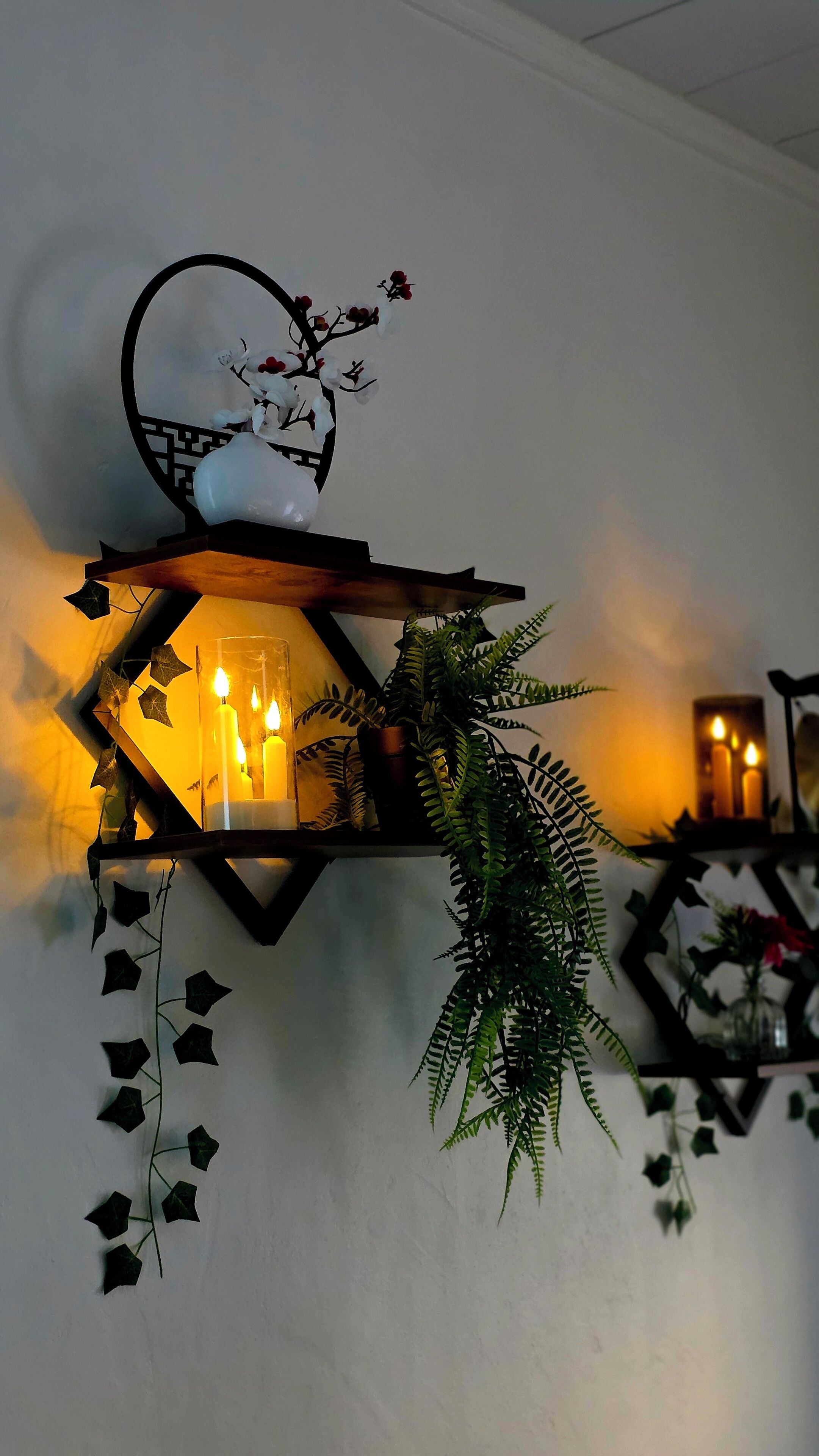 A wall-mounted lantern with candles, a decorative flower, and a potted plant.