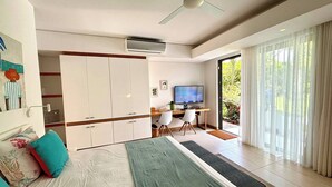 Een slaapkamer met een bed, een bureau met een computer, een televisie en een schuifdeur naar een balkon.