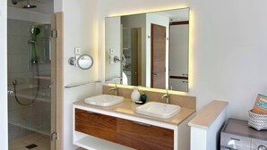 Een moderne badkamer met een douche met glazen wand, een dubbele wastafel en een Samsung wasmachine.