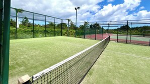 Een tennisbaan buiten met een net, omringd door groen hekwerk en bomen.