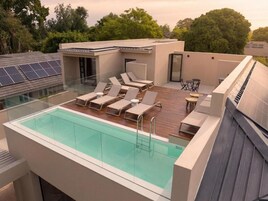 Una piscina en la azotea con sillones de descanso, una terraza de madera y paneles solares.