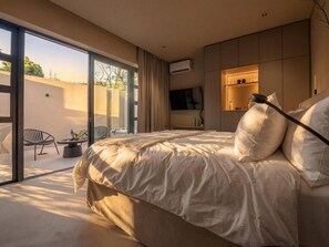 A modern bedroom with a large bed, a TV, and a sliding glass door leading to an outdoor area.