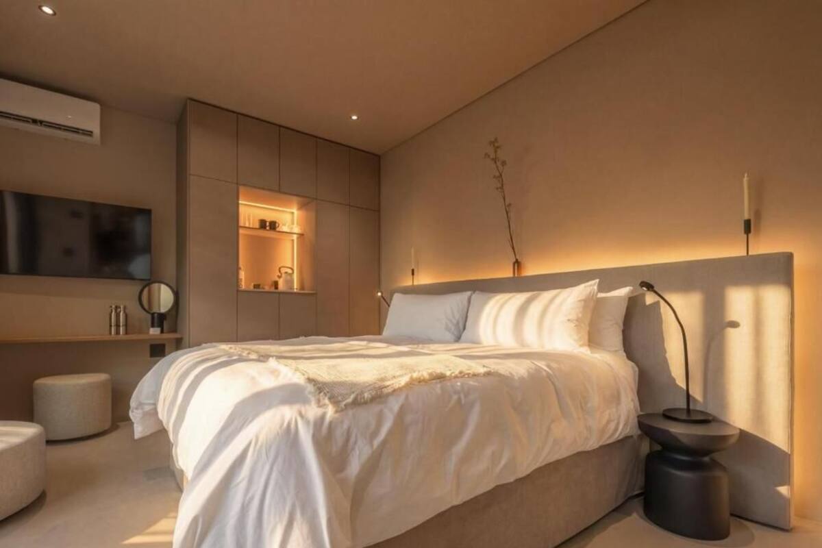 A modern bedroom with a large bed, bedside tables, a flat-screen TV, and built-in shelving.