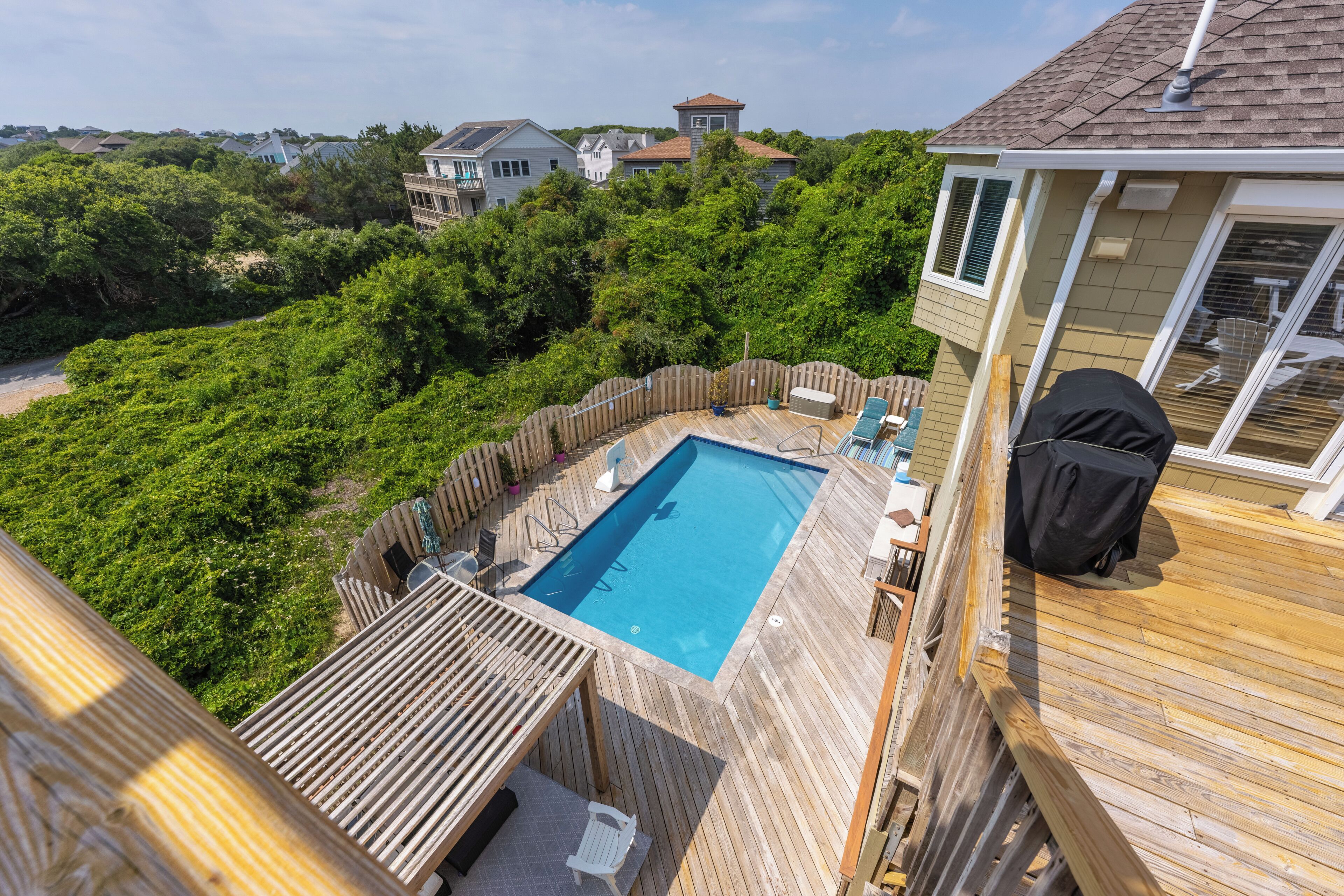 Un jardin avec une piscine, une terrasse en bois et un espace barbecue couvert.