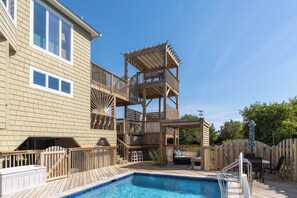 Ein Garten mit Swimmingpool, Holzterrasse und einer mehrstöckigen Holzkonstruktion mit Geländern.