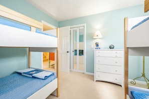A bunk bed room with a white dresser, a door leading to another room, and a lamp on a side table.