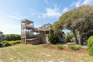 A multi-story wooden structure with a balcony, a stone tower, and a large tree in the yard.