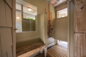 A bathroom with a wooden bench, a mirror, and a shower area.
