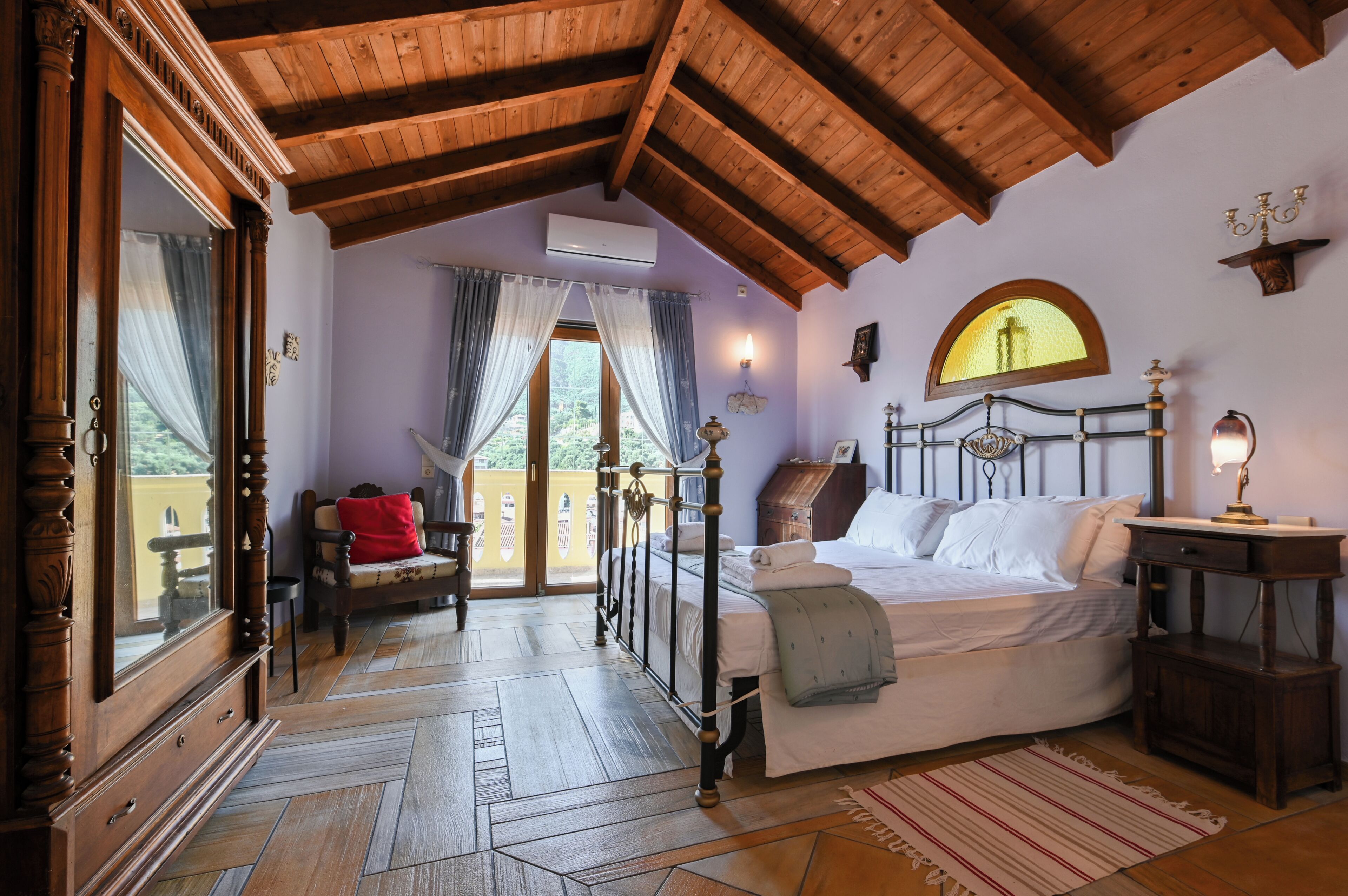 Ein Zimmer mit Bett, Holzbalkendecke, einem Vorhangfenster, einem Sessel und einem kleinen Tisch.