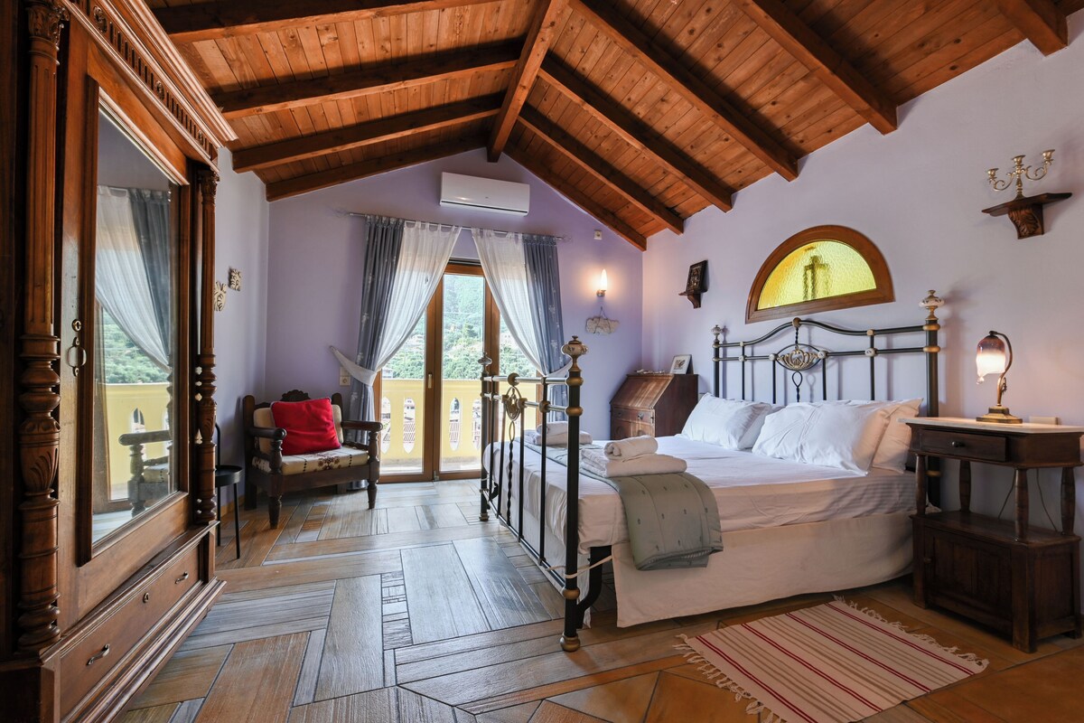 Ein Zimmer mit Bett, Holzbalkendecke, einem Vorhangfenster, einem Sessel und einem kleinen Tisch.