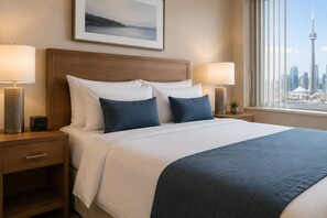 Ein Hotelzimmer mit einem großen Bett, zwei Nachttischlampen, einem Nachttisch, einer Schublade, einem gerahmten Bild an der Wand und einem Fenster mit Blick auf die Stadt.