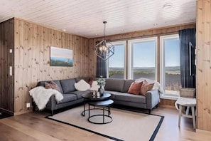 A living room with a wooden interior, a sofa set, a coffee table, and large windows with a view.