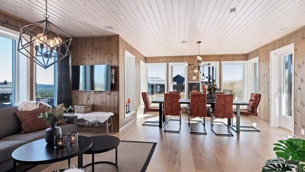A spacious living area with a wooden ceiling, a fireplace, a dining area with chairs, and a large window offering a view.