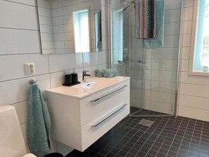 Et moderne badeværelse med et hvidt skab, en brusekabine med glasdøre og et stort spejl.
