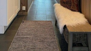 A hallway with wooden walls, a bench with a fur throw, and a patterned rug.