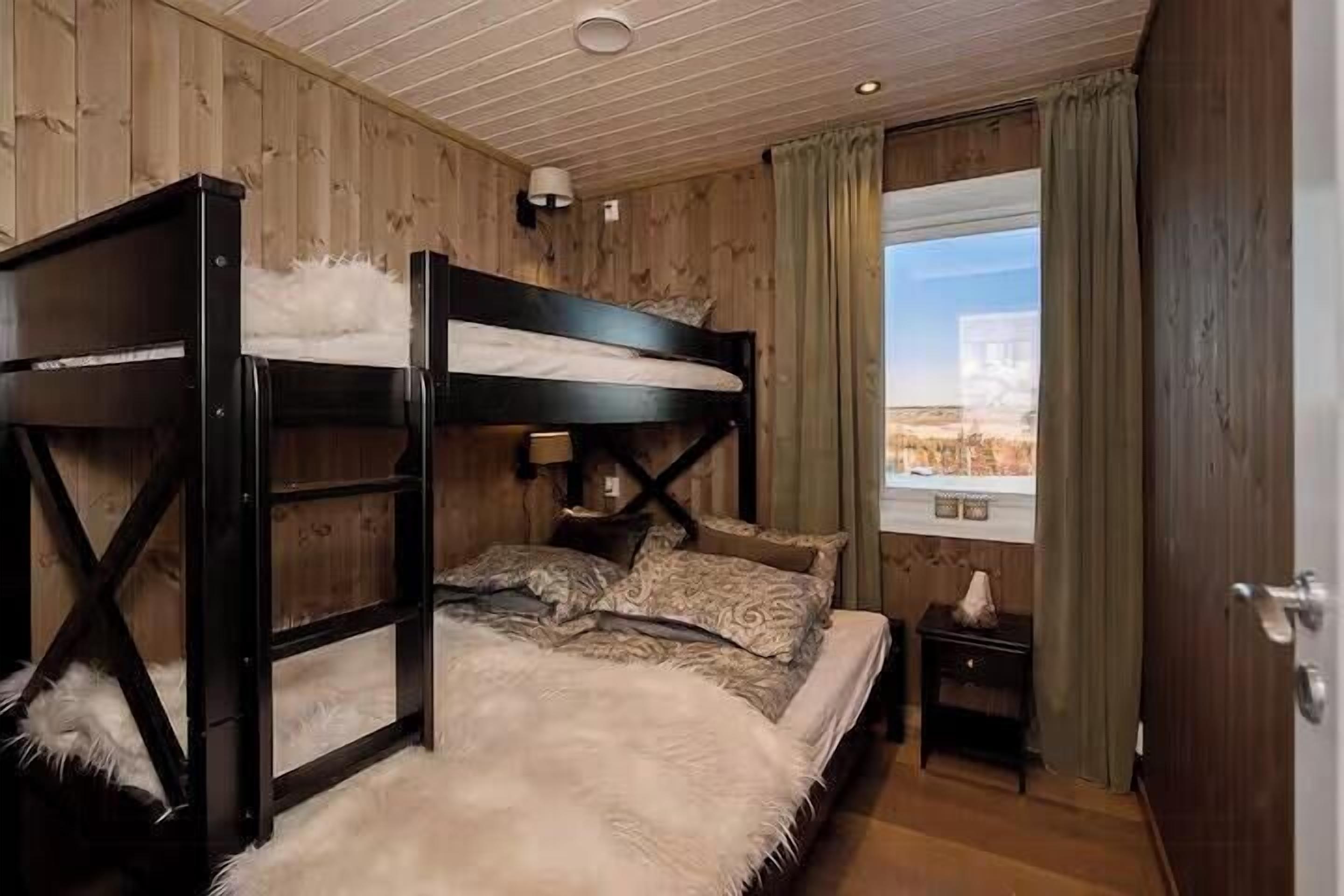 A bunk bed room with a window view, wooden walls, and a small bedside table.