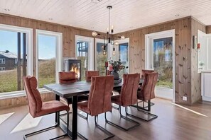 A dining room with a wooden paneled wall, a central fireplace, and a large window.