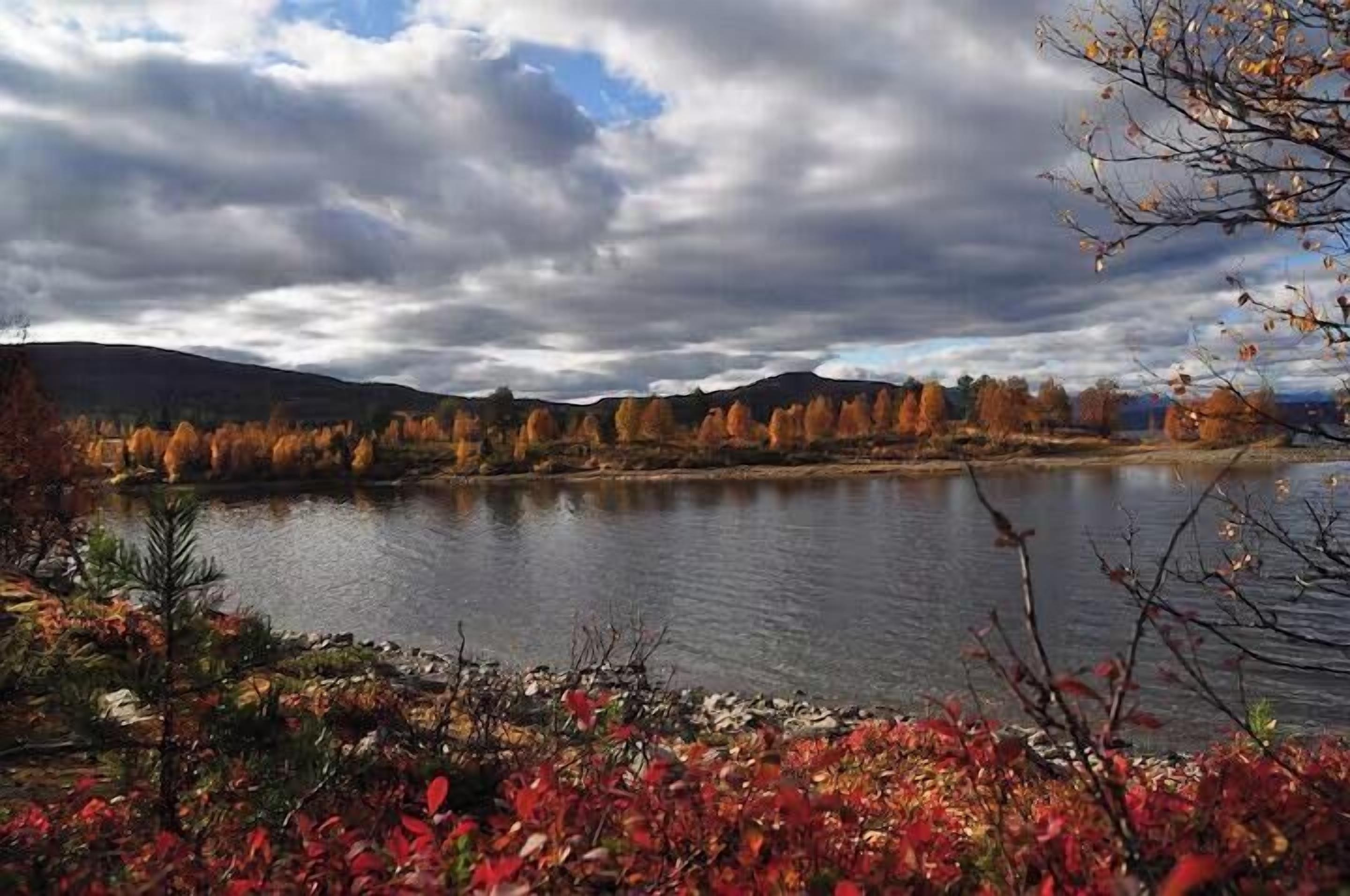 Un lac bordé d’un feuillage automnal, un ciel dégagé et des collines lointaines.