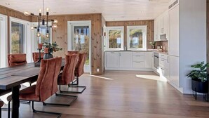 A modern kitchen with white cabinets, a dining area with a wooden table and chairs, and a ceiling with exposed beams.