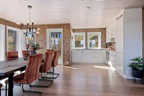 A modern kitchen with white cabinets, a dining area with a wooden table and chairs, and a ceiling with exposed beams.