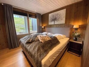 Et soveværelse med en stor seng, trævægge, et vindue og et natbord med en lampe.