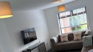 Una sala de estar moderna con un sofá, un televisor montado en la pared, una mesa de comedor con sillas y una ventana con persianas.