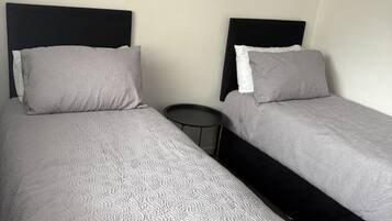 Two single beds with black headboards, grey bedding, and a small round table between them.