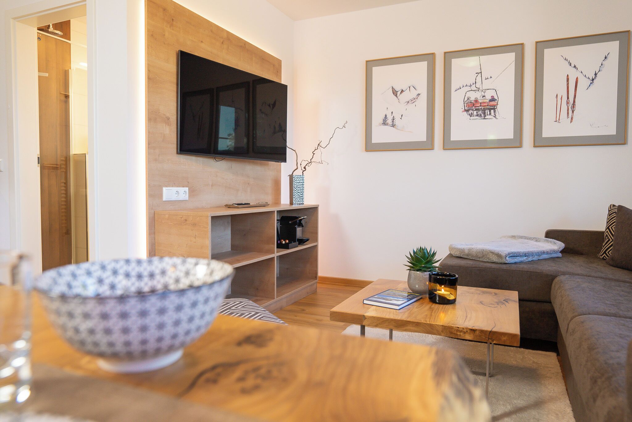Un salon moderne avec un meuble TV en bois, une table basse, un canapé et des œuvres d’art encadrées accrochées au mur.