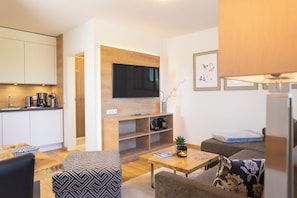 Ein modernes Wohnzimmer mit Fernseher, einer Kaffeemaschine, einem Bücherregal und einem Sofa.