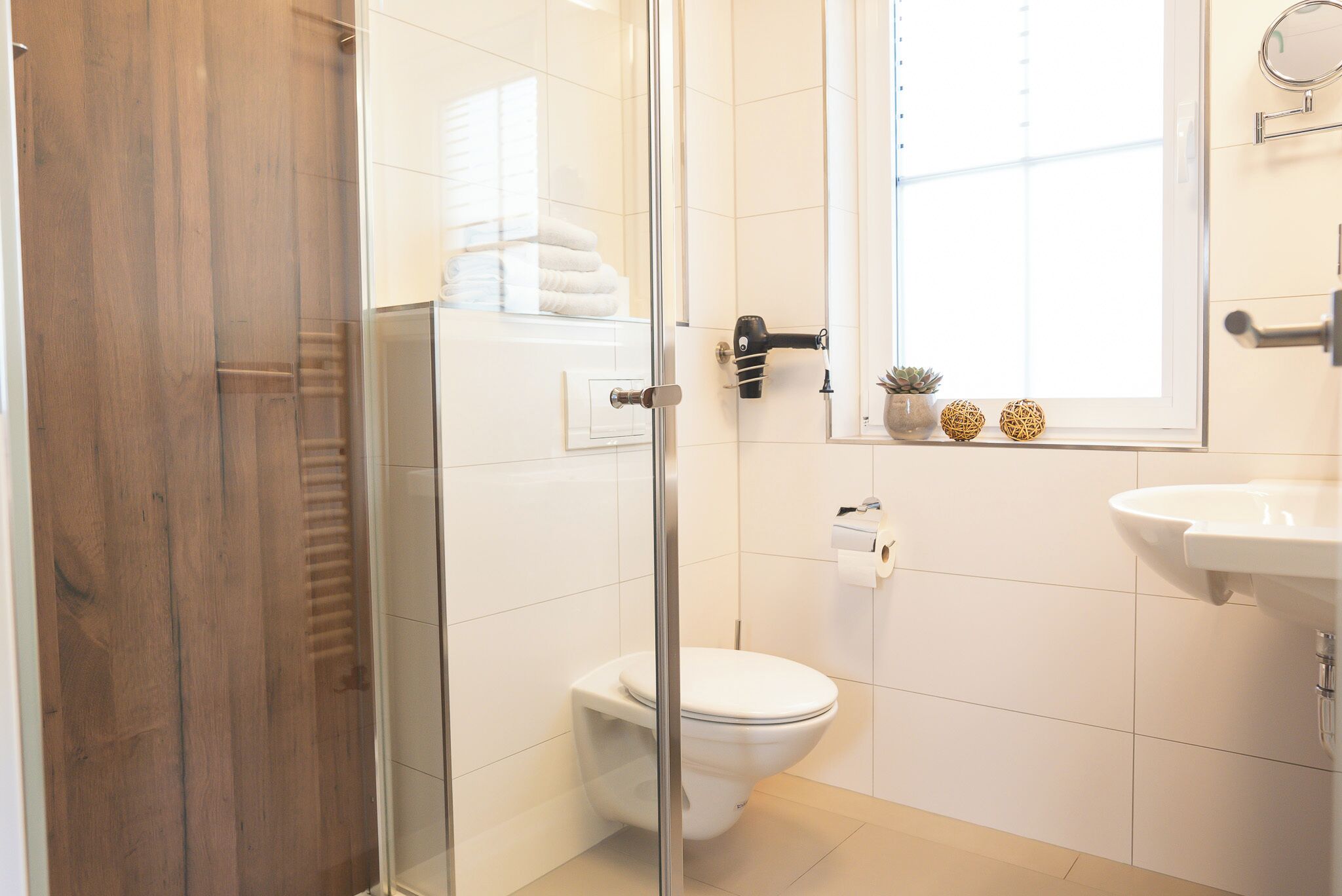 Un baño moderno con cabina de ducha de vidrio, inodoro blanco, lavamanos y ventana con luz natural.